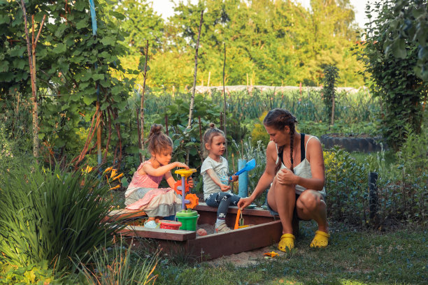 快乐的孩子们和妈妈一起在公园里绿树成荫的沙箱里玩耍，作为大家庭的生活方式，象征着快乐的童年图片下载