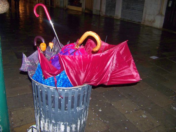 意大利威尼斯，在一个风雨过后的夜晚，灰色的公共垃圾桶被强风吹碎，不同颜色和类型的雨伞。图片下载