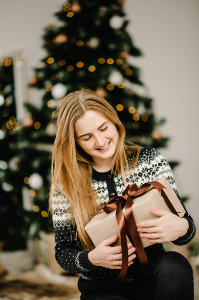 圣诞节时尚照片美丽的女孩与金发在舒适的衣服摆pose在圣诞树与礼物盒。新年快乐理念。图片下载