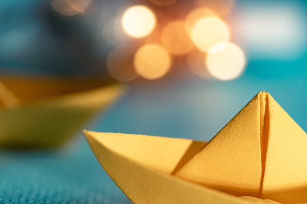 用蓝色纸在海上折纸的黄色帆船。纸张艺术风格的背景与船，海洋和散景灯图片下载