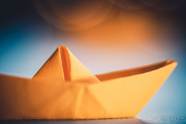 用蓝色纸在海上折纸的黄色帆船。纸张艺术风格的背景与船，海洋和散景灯图片下载