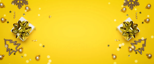 圣诞节销售。白色的礼物与金色的蝴蝶结，黄色的球和闪闪发光的灯在圣诞节装饰在黄色的背景贺卡。圣诞节，冬天，新年的概念。图片下载