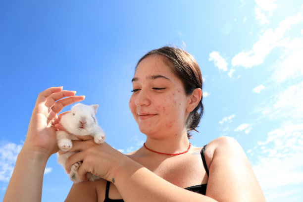 一个十几岁的女孩在晴朗的天空中抱着兔子宝宝图片下载