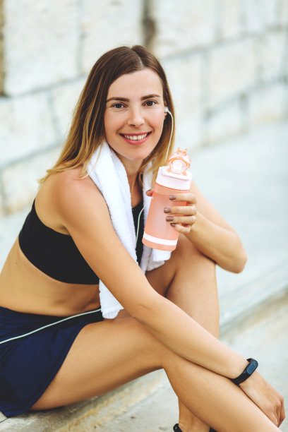 健身的女人喝瓶子里的水。肌肉发达的年轻女性在外面休息。图片下载