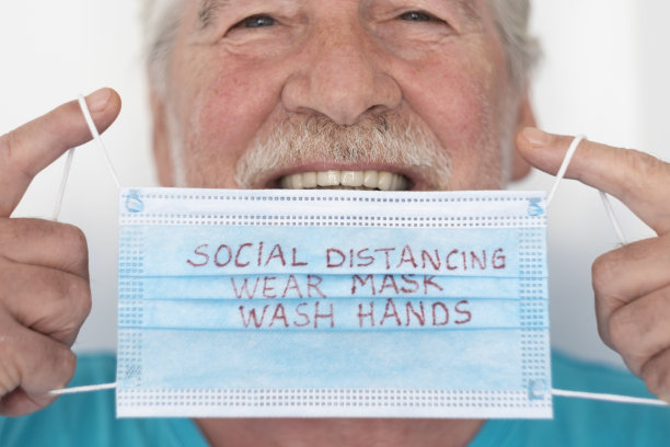 冠状病毒特写镜头:戴着医用口罩的老人微笑着，上面写着避免冠状病毒感染的信息——退休老人的概念和全球病毒警报图片下载