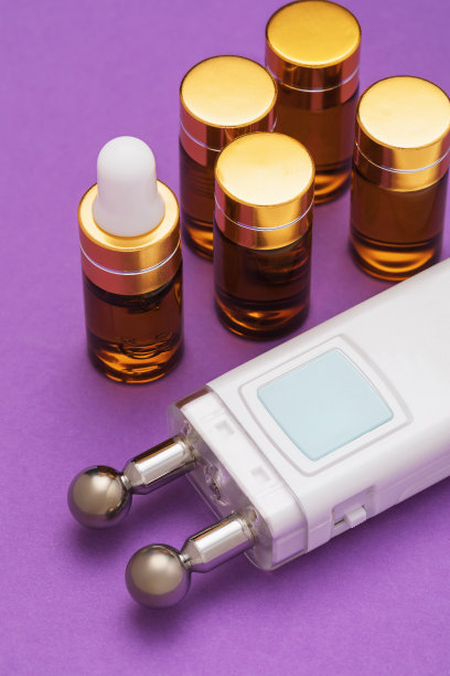 一套安瓿中的凝胶和一个在紫色背景下对面部肌肉进行微电流刺激的装置图片下载