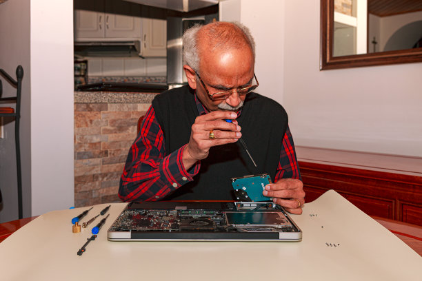 一个72岁的亚洲印度人，业余，有一个Movember胡子看到修理他的笔记本电脑在家里，做一个内部硬盘升级-特写图片下载