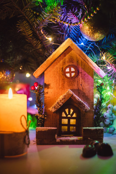 模糊的绿色圣诞树背景上是一个里面亮着灯的小玩具圣诞屋。房地产，节日，圣诞节，迷你。背景明信片图片下载