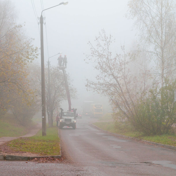 危险工作的概念。垂直照片员工工人在橙色正装制服站在升降机桶更换灯泡或灯在柱上对上模糊的城市背景图片下载