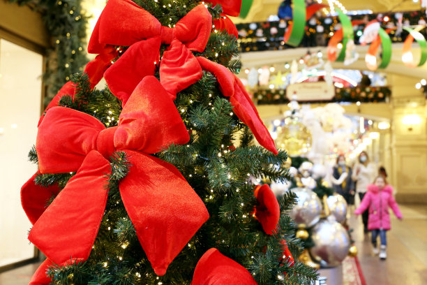 圣诞树用红色的节日蝴蝶结在购物中心的节日灯和行人的背景图片下载