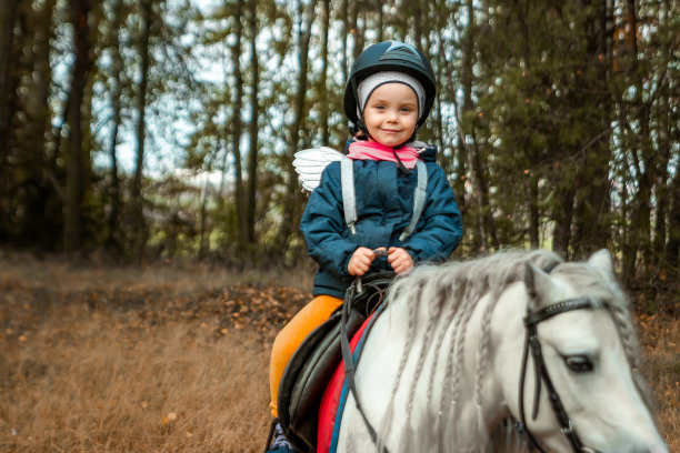 小女孩骑着一匹白马，站在大自然的背景上。骑师，竞技场，骑马。图片下载