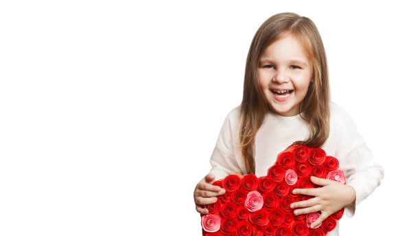 快乐可爱的笑着的小女孩，一个在白色背景上用红色大纸做心形的学龄前儿童。图片下载