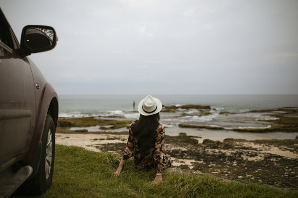 亚洲人坐在汽车的前轮享受巴厘岛的海滩图片下载