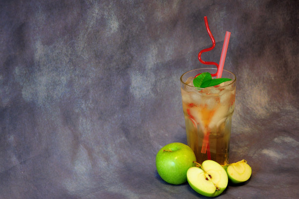 一杯绿苹果汁加冰，吸管和成熟的水果在灰色的背景。图片下载