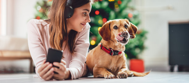 一个十几岁的女孩和她的狗躺在圣诞树旁的地板上听音乐图片下载