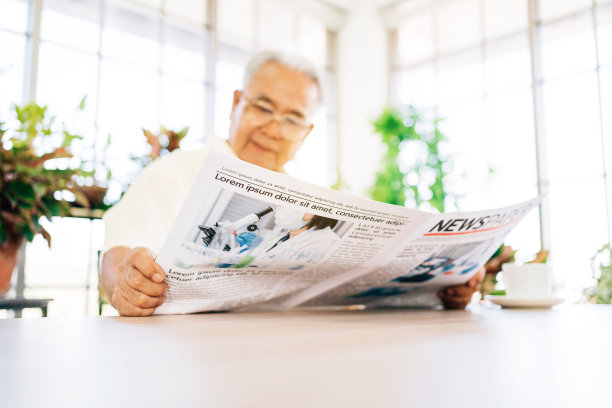 一位身着便装的退休老人正在关注阅读有关COVID-19的报纸。坐在家里，有一个室内花园。退休后的爱好和生活方式。图片下载