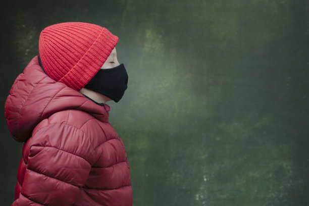 男孩戴着防冠状病毒的黑色安全口罩，穿着冬季夹克和红色帽子。侧视图。Covid-19在全球爆发图片下载