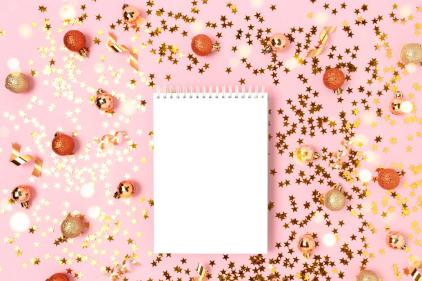 粉色背景的笔记本模型，金色的五彩纸屑和圣诞小玩意。图片下载