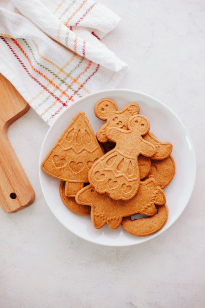 新鲜出炉的姜饼放在白色的盘子里，放在白色的餐桌上，配上木制的砧板和白色、红色和绿色的毛巾。图片下载