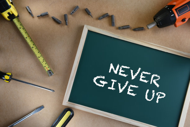 永远不要放弃用工具在棕色背景的黑板上写字。图片下载