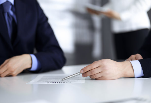 商务人士在会议或谈判中讨论合同，坐在一起，背景是一个不认识的女人，特写。一群不知名的商人在一个现代化的办公室里。团队合作、伙伴关系的概念图片下载