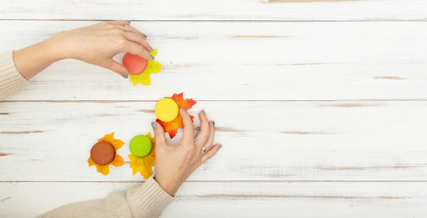 马卡龙蛋糕和女性的手美甲在白色的木制背景。秋叶谎言。图片下载