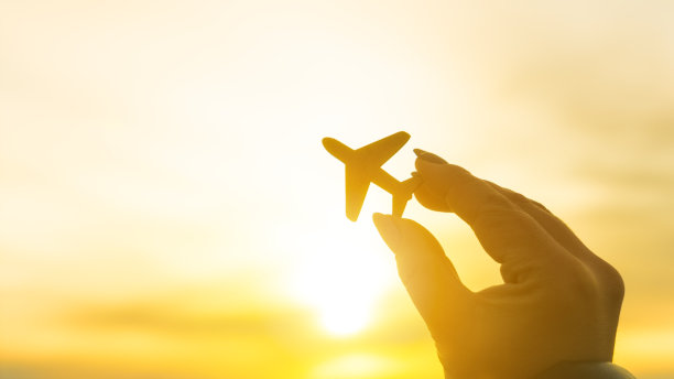 日落背景上一只手握着一架飞机的剪影。图片下载