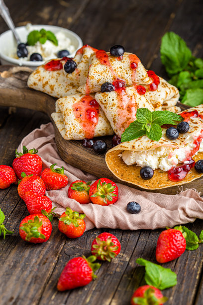 白软干酪裹在薄饼里，还有浆果、草莓、蓝莓、薄荷、果酱，上面和旁边的照片，放在一个木制砧板上，在一个黑暗的孤立的背景上图片下载