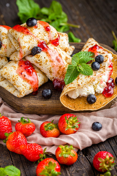 白软干酪裹在薄饼里，还有浆果、草莓、蓝莓、薄荷、果酱，上面和旁边的照片，放在一个木制砧板上，在一个黑暗的孤立的背景上图片下载
