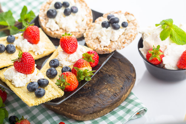 几块薄脆饼干上放白干酪，草莓薯片，草莓蓝莓和薄荷，上面和旁边的照片，在一个木制砧板上，在一个白色孤立的背景上图片下载