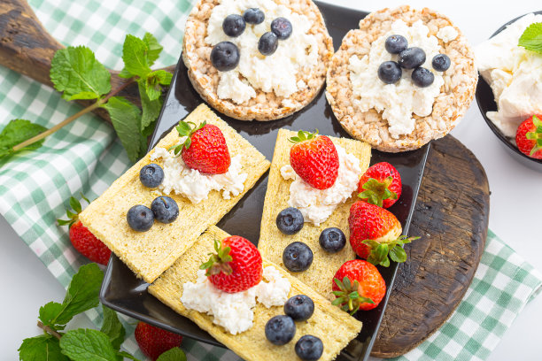 几块薄脆饼干上放白干酪，草莓薯片，草莓蓝莓和薄荷，上面和旁边的照片，在一个木制砧板上，在一个白色孤立的背景上图片下载