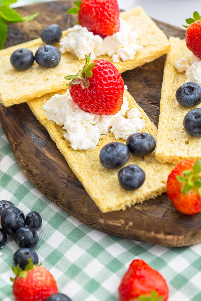 几块薄脆饼干上放白干酪，草莓薯片，草莓蓝莓和薄荷，上面和旁边的照片，在一个木制砧板上，在一个白色孤立的背景上图片下载