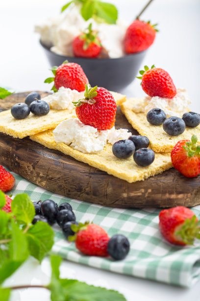 几块薄脆饼干上放白干酪，草莓薯片，草莓蓝莓和薄荷，上面和旁边的照片，在一个木制砧板上，在一个白色孤立的背景上图片下载