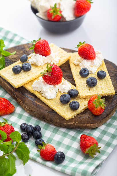 几块薄脆饼干上放白干酪，草莓薯片，草莓蓝莓和薄荷，上面和旁边的照片，在一个木制砧板上，在一个白色孤立的背景上图片下载