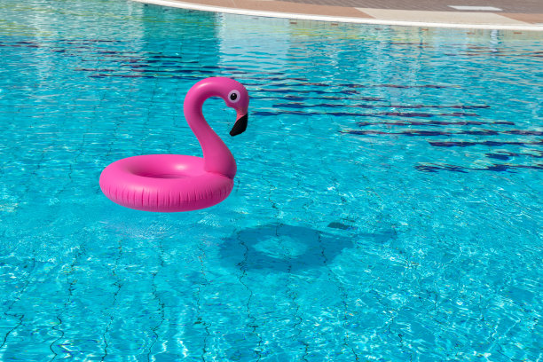 夏天的乐趣。粉红色的充气火烈鸟在游泳池的水为夏天的海滩背景。奢侈的生活方式。图片下载
