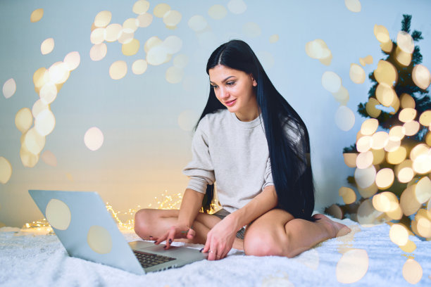 一个年轻漂亮的女孩在新年前在家里用电脑通过互联网订购礼物。图片下载