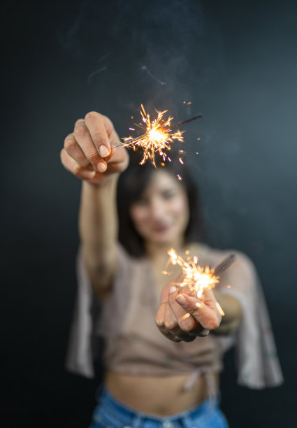 特写照片的愉快的白人女孩拿着孟加拉灯。快乐的年轻女子的肖像在红色睡衣孤立的黑色背景与火花图片下载