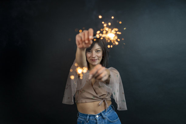 特写照片的愉快的白人女孩拿着孟加拉灯。快乐的年轻女子的肖像在红色睡衣孤立的黑色背景与火花图片下载
