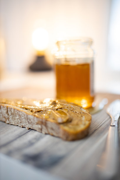 木桌上放着一片涂着花生酱的面包和一个蜂蜜罐图片下载