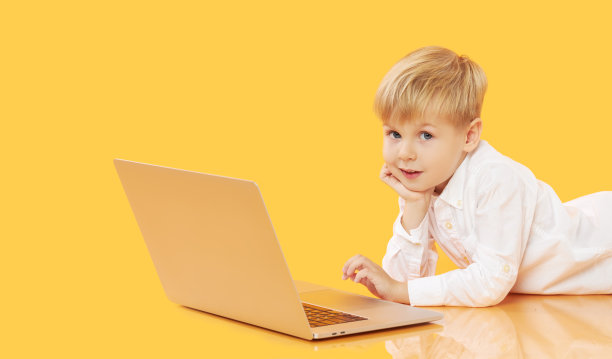 一个小男孩用黄色背景的笔记本电脑。教育，在线学习，在家学习，远程学习。隔离期间的小学生图片下载
