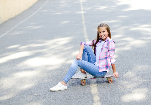 可爱的小女孩坐在滑板上。十几岁的孩子在户外吃便宜货图片下载