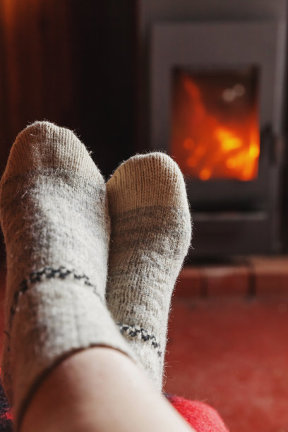脚腿在冬天的衣服羊毛袜子在壁炉的背景。女人坐在家里在冬秋的晚上放松和热身。冬季和寒冷天气概念。Hygge圣诞夜图片下载