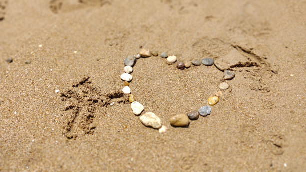 在seesa海滩的沙子上，手工摆放着心形的石头图片下载