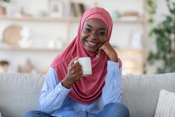 放松的喝。微笑的黑人穆斯林妇女戴着头巾在家喝咖啡图片下载
