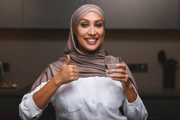 在厨房里拿着一杯水并竖起大拇指的穆斯林妇女图片下载