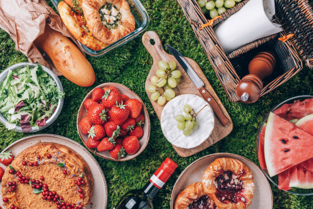 野餐草篮，健康食品，配件。夏日野餐，蛋糕，水果，奶酪，葡萄酒和零食，格子在绿色的背景。前视图。副本的空间。夏天的家庭午餐。浪漫野餐图片下载
