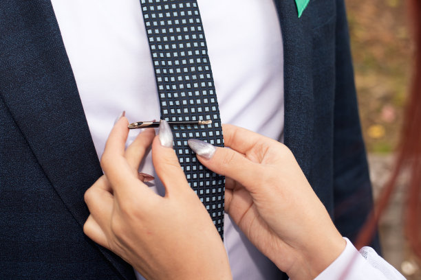 新娘把夹子夹在新郎的领带上。新郎婚礼当天的费用、传统的准备和组织图片下载