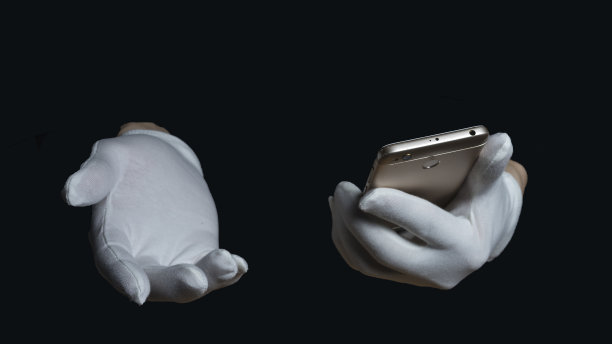 双手戴白手套，背景是黑色。一只手拿着智能手机，另一只手在黑色背景上制作请帖图片下载