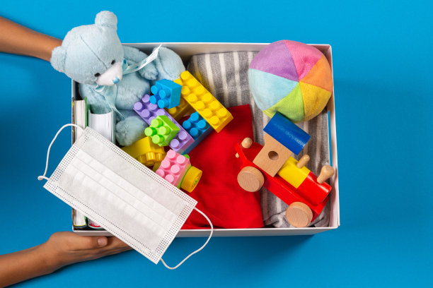 捐赠的概念。孩子的手与捐赠箱，衣服，书籍和玩具在浅蓝色的背景。俯视图图片下载