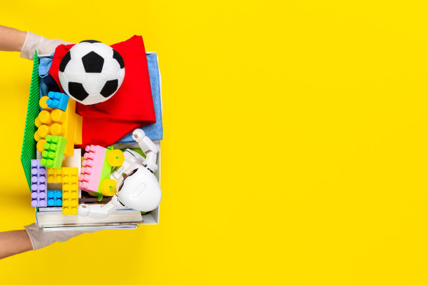 捐赠的概念。手拿手套的女人拿着捐赠箱，里面有黄色背景的衣服、书籍和玩具。俯视图图片下载